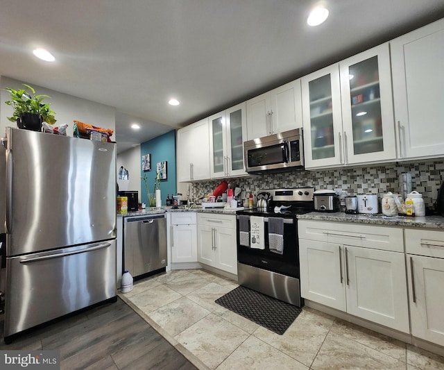 kitchen featuring backsplash, light stone counters, appliances with stainless steel finishes, and white cabinetry