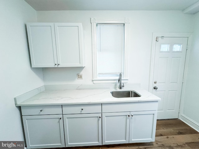 kitchen featuring hardwood / wood-style floors, sink, light stone countertops, and white cabinets