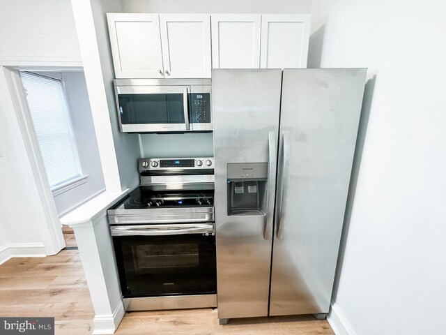 kitchen with light wood-type flooring, appliances with stainless steel finishes, and white cabinetry