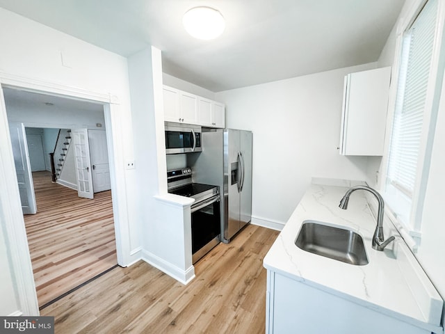 kitchen with light wood-style flooring, appliances with stainless steel finishes, light stone counters, white cabinetry, and a sink