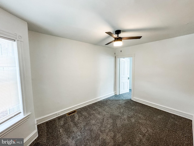 empty room with visible vents, dark carpet, baseboards, and ceiling fan