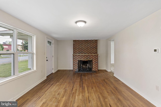 unfurnished living room with wood-type flooring, brick wall, and a fireplace