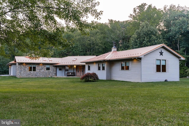 rear view of house featuring metal roof, stone siding, a lawn, and a chimney