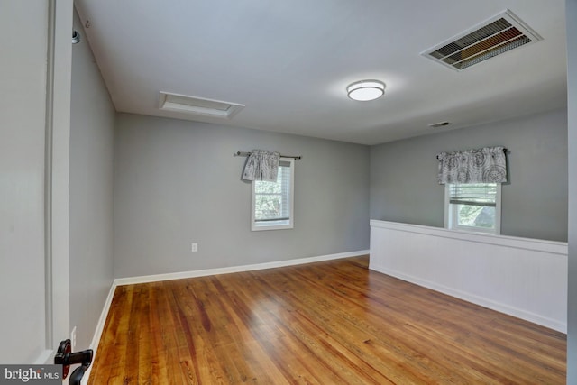 empty room with attic access, a healthy amount of sunlight, visible vents, and wood finished floors