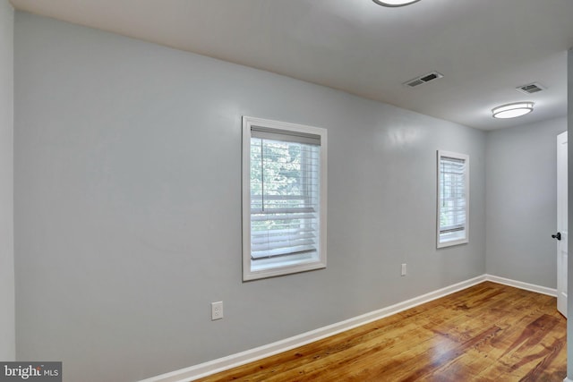 spare room with baseboards, wood finished floors, visible vents, and a healthy amount of sunlight