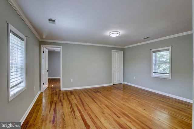 empty room featuring ornamental molding, light wood-style flooring, visible vents, and baseboards