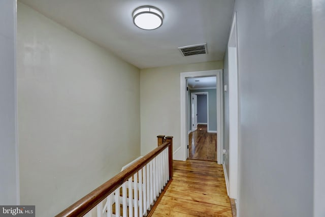 corridor with light wood-style floors, visible vents, and an upstairs landing