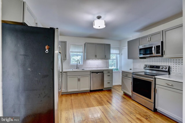 kitchen with backsplash, sink, light hardwood / wood-style flooring, stainless steel appliances, and gray cabinets