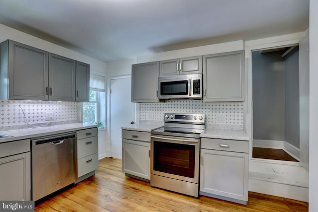 kitchen with appliances with stainless steel finishes, light wood-type flooring, and decorative backsplash