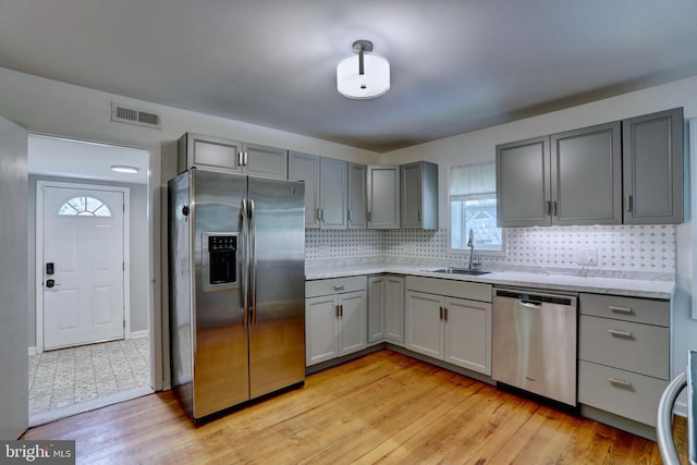 kitchen with backsplash, gray cabinets, appliances with stainless steel finishes, light hardwood / wood-style floors, and sink