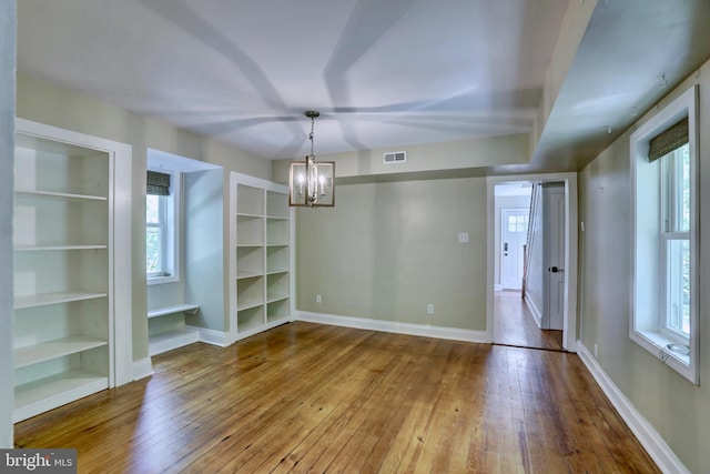 unfurnished dining area with visible vents, a notable chandelier, baseboards, and wood finished floors