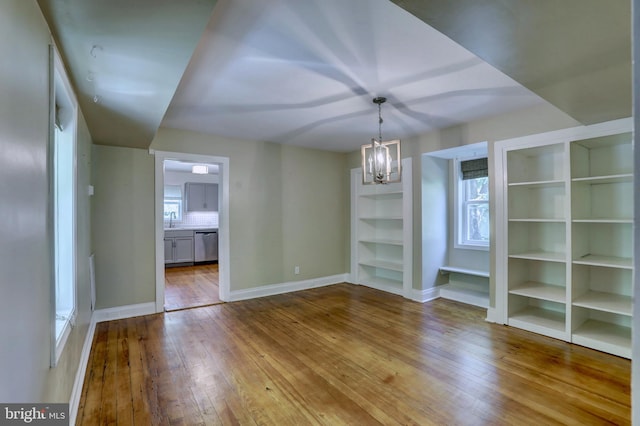 unfurnished dining area featuring light wood-type flooring, baseboards, a chandelier, and a sink