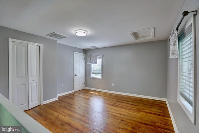 empty room featuring baseboards, wood finished floors, visible vents, and attic access