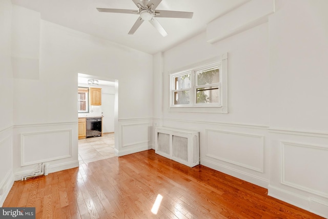 empty room with light hardwood / wood-style floors, ceiling fan, and wine cooler