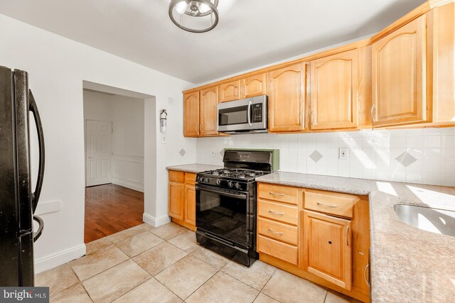 kitchen featuring black appliances, tasteful backsplash, light stone countertops, light brown cabinetry, and light wood-type flooring