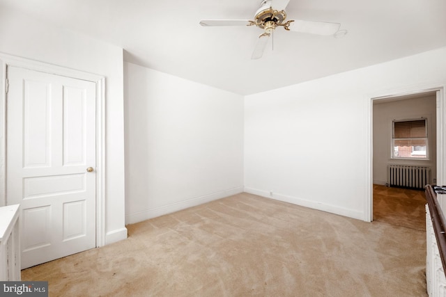 spare room featuring radiator heating unit, ceiling fan, and light colored carpet