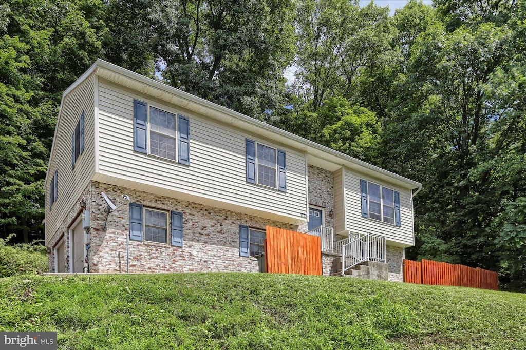 bi-level home with a garage, brick siding, stone siding, fence, and a front yard