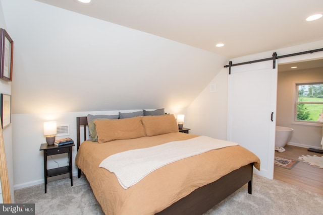 bedroom with ensuite bath, vaulted ceiling, a barn door, and light hardwood / wood-style floors