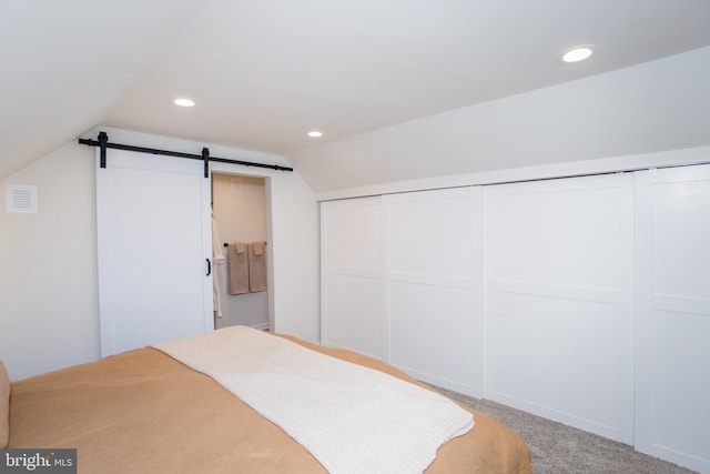 carpeted bedroom with a barn door, vaulted ceiling, and a closet