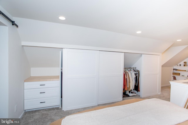 carpeted bedroom featuring vaulted ceiling, a barn door, and a closet