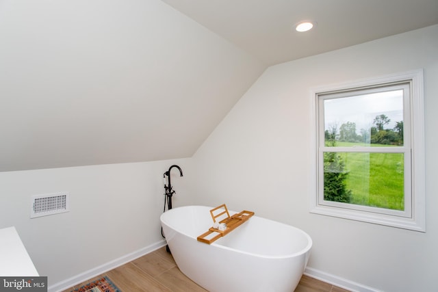 bathroom featuring a tub, vaulted ceiling, and hardwood / wood-style flooring