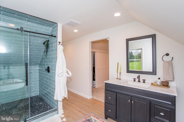 bathroom featuring vanity, vaulted ceiling, hardwood / wood-style floors, and a shower with shower door