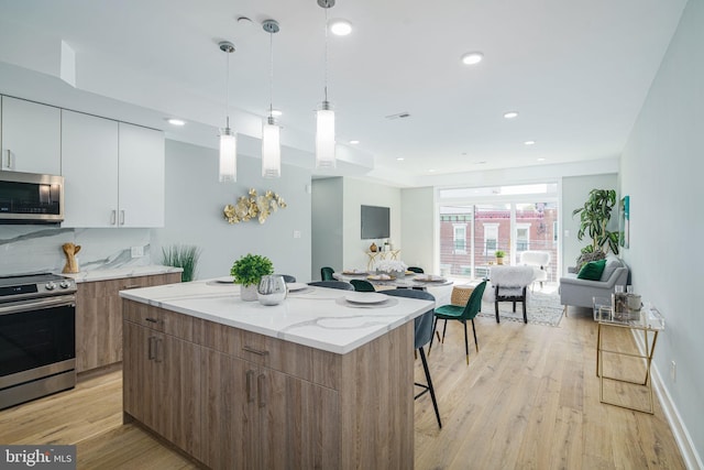 kitchen with light wood-type flooring, a kitchen island, white cabinets, a breakfast bar, and appliances with stainless steel finishes