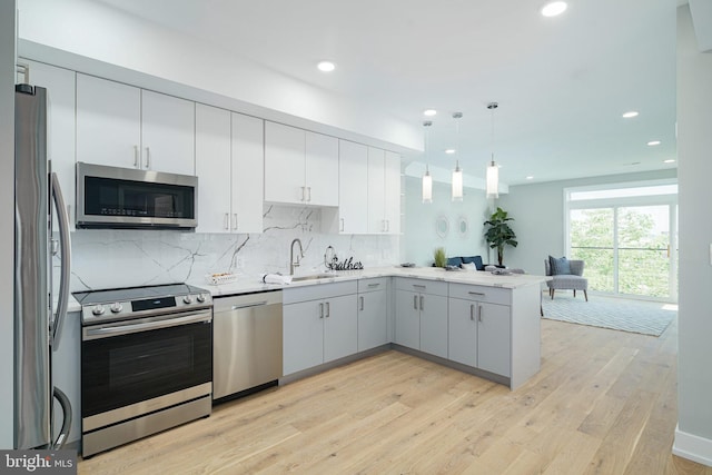 kitchen with light wood-type flooring, kitchen peninsula, hanging light fixtures, sink, and appliances with stainless steel finishes