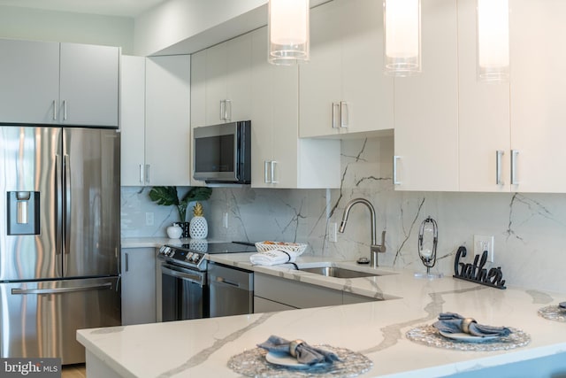 kitchen featuring white cabinetry, hanging light fixtures, stainless steel appliances, sink, and light stone counters