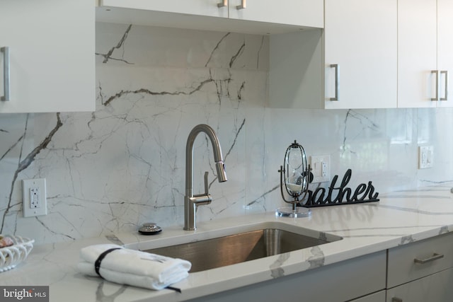 kitchen with white cabinetry, sink, light stone counters, and decorative backsplash