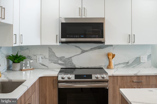 kitchen featuring white cabinets, stainless steel appliances, backsplash, and light stone countertops