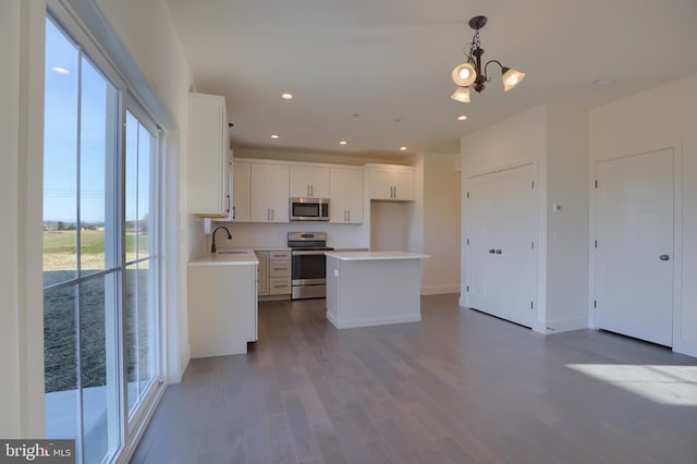 kitchen featuring appliances with stainless steel finishes, white cabinetry, sink, wood-type flooring, and a kitchen island