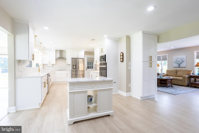 kitchen with wall chimney exhaust hood, a center island, stainless steel appliances, white cabinetry, and a sink