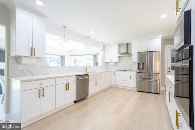 kitchen with backsplash, appliances with stainless steel finishes, light hardwood / wood-style floors, white cabinetry, and wall chimney range hood