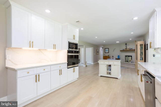 kitchen with appliances with stainless steel finishes, light hardwood / wood-style flooring, backsplash, light stone countertops, and white cabinets