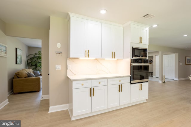 kitchen with white cabinetry, light wood-type flooring, backsplash, and appliances with stainless steel finishes