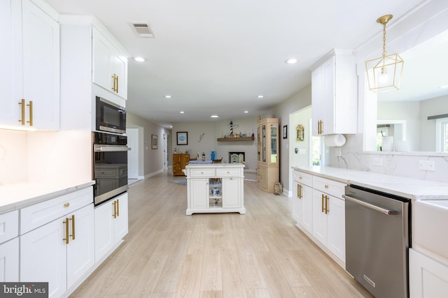 kitchen featuring light wood-type flooring, black microwave, stainless steel dishwasher, hanging light fixtures, and oven