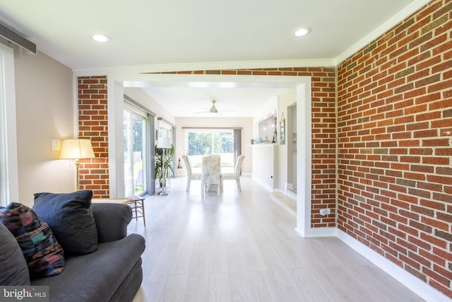 living area featuring light wood-style floors, brick wall, baseboards, and crown molding