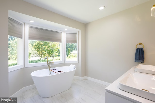 full bath featuring marble finish floor, a freestanding bath, baseboards, and double vanity