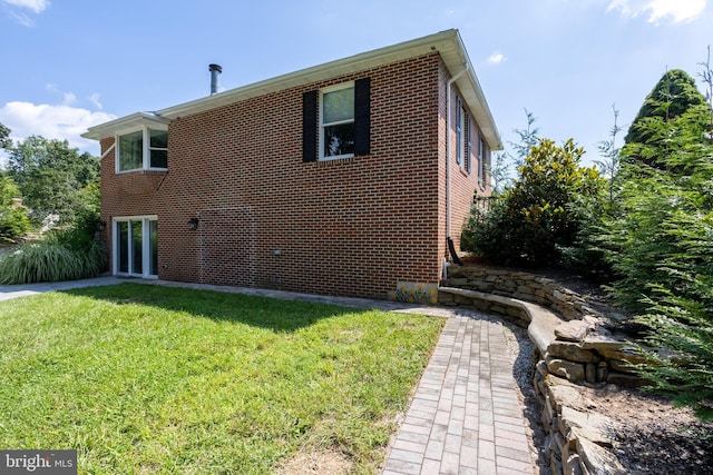 back of house featuring brick siding and a lawn