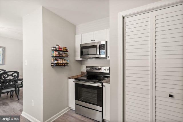 kitchen with stainless steel appliances, white cabinetry, and light hardwood / wood-style floors