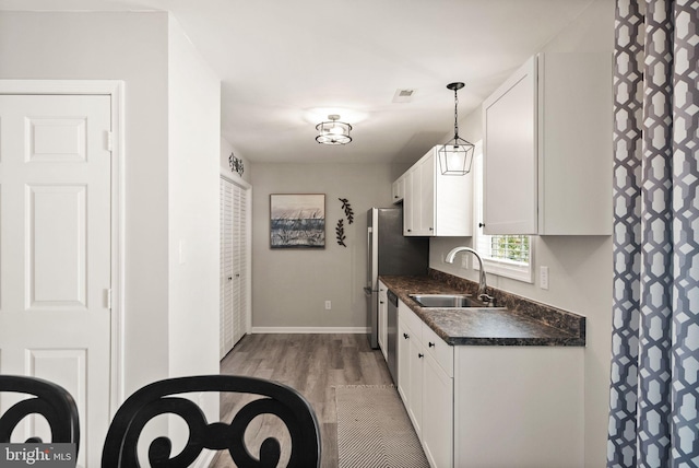 kitchen featuring decorative light fixtures, light hardwood / wood-style floors, stainless steel dishwasher, sink, and white cabinetry