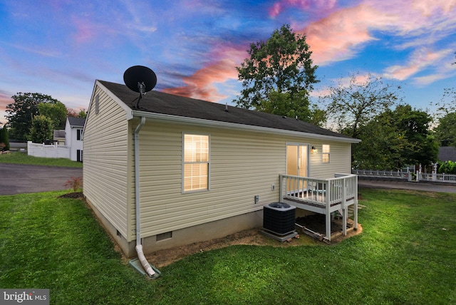 back house at dusk featuring a yard and central AC unit