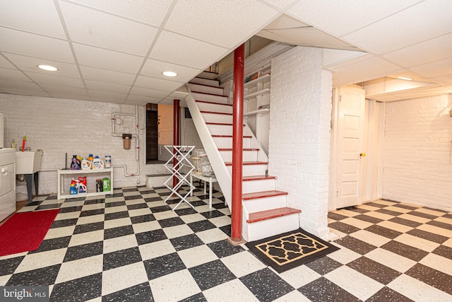 basement featuring brick wall, tile patterned floors, and a drop ceiling