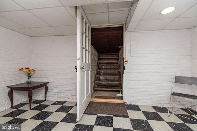 stairway featuring a paneled ceiling and brick wall