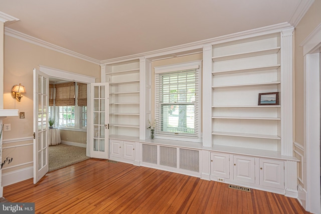 unfurnished living room featuring built in shelves, wood-type flooring, crown molding, and french doors