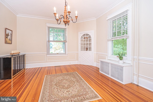 unfurnished dining area with radiator heating unit, ornamental molding, wood-type flooring, and an inviting chandelier