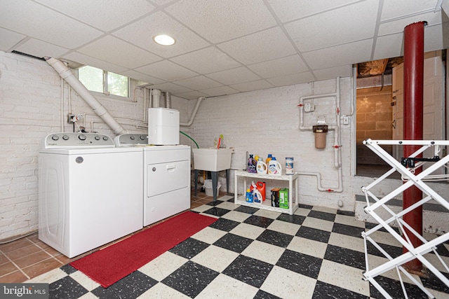 laundry room with light tile patterned floors, washing machine and clothes dryer, and brick wall