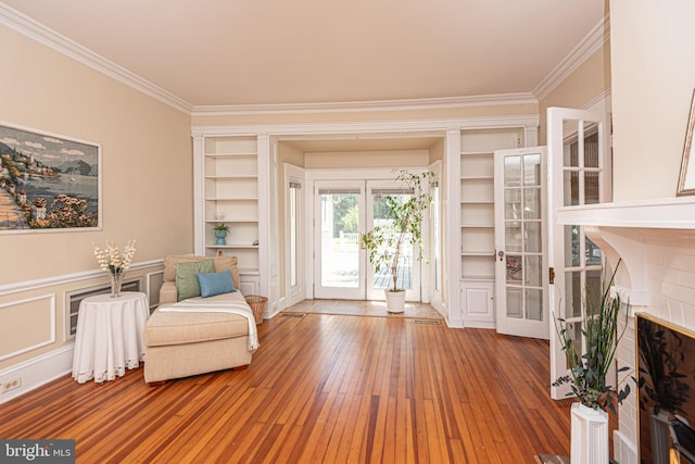 sitting room featuring french doors, ornamental molding, a brick fireplace, and hardwood / wood-style flooring