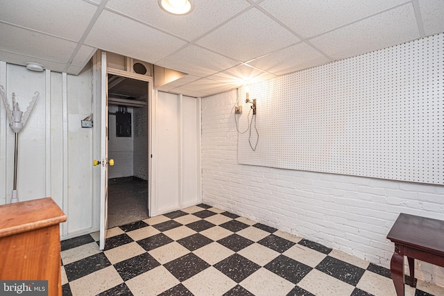 basement featuring brick wall and a drop ceiling